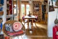 Cozy living room with wicker chair, colorful cushions, and view into dining area with wooden table and brick wall.