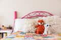Pink metal bed with ruffled pillows, orange fox, and white tiger plush toys on a colorful patchwork quilt.