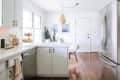 Bright kitchen with white cabinets, stainless steel fridge, wooden floor, and a small dining area with a round table and chairs.