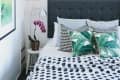 Bedroom with a gray headboard, tropical leaf pillows, orchid plant, and geometric wall decor.