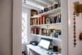 Home office with a white desk, computer, printer, and shelves filled with books and decorative items.
