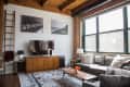 Loft living room with a gray sofa, wooden TV stand, large windows, and a patterned rug.