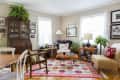 Cozy living room with patterned rug, wooden furniture, plants, and framed photos on beige walls.