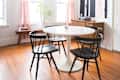 Dining room with round white table, four black chairs, wood floor, red curtains, and abstract wall art.
