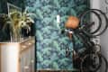Floral rug, tropical wallpaper, wooden cabinet with vase, and wall-mounted bicycle in a narrow hallway.