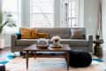 Gray sofa with patterned cushions, wooden coffee table, and decor in a bright living room with large windows and a plant.