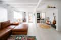 Open living room with brown leather sectional, colorful rug, wood stove, and guitars in the corner near a desk.