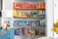 Color-coded bookshelf with red, yellow, green, blue, and black books, next to a blue dresser with a lamp and decor.
