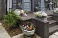 Gray wooden house with ornate trim, potted flowers, and a small porch with metal chairs and a table.