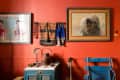 Eclectic room with red walls, framed art, textiles, a blue chair, and a guitar leaning against a vintage cabinet.