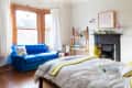 Bright bedroom with blue sofa, wooden shelves, potted plants, and a decorative fireplace.