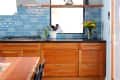 Modern kitchen with wooden cabinets, blue tile backsplash, black countertop, and a vase of yellow flowers.