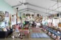 Eclectic living room with colorful armchairs, long wooden dining table, vibrant wall art, and ceiling fans.