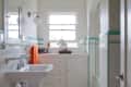 Narrow bathroom with pedestal sink, orange towel, white cabinets, and turquoise tile accents.