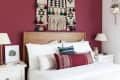 A burgundy accent wall behind a bed with white fluffy bedding and a wood bed frame