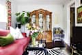 Living room with red sofa, green pillows, floral curtains, wooden cabinet, zebra rug, and a bouquet of flowers on a glass table.