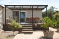 Wooden deck with pergola, outdoor dining set, potted plants, and sliding glass doors leading to a house.