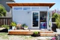 Small modern studio with wooden deck, open glass doors, potted plants, and colorful decor inside.