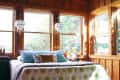 Cozy bedroom with wood paneling, large windows, polka dot bedspread, and hanging pendant lights.
