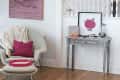 Cozy living room with a white chair, pink pillow, knitted throw, pink rabbit artwork, and a decorative console table.