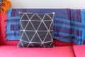 Red sofa with a geometric black and white pillow, blue throw, and eclectic wall art including a framed portrait and landscape.