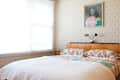 Bedroom with a wooden bed, white quilt, patterned wallpaper, green pendant light, and a portrait on the wall.