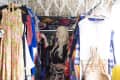 Woman browsing colorful dresses in a vibrant, eclectic closet with patterned wallpaper and a red rug.