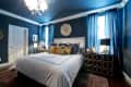 Elegant bedroom with dark blue walls, white bedding, leopard print pillows, and gold-accented dresser under blue curtains.