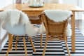 A dining room table on checkerboard flooring with sheepskin rugs on the chairs.