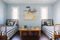Two twin beds with checkered bedding in a blue room, toy planes hanging above, and a map on the wall.
