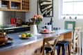 Wooden kitchen island with bar stools, geometric floor tiles, hanging lights, and a vase of flowers.