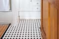 Bathroom with black and white tile floor, white vanity, potted plant, and wooden door.
