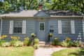 Blue house with white shutters, front door, and flower garden, surrounded by trees.