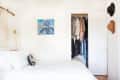 A minimalist white bedroom with colorful wall decor and hats hanging on the wall as well as an open closet full of clothes.