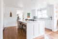 Bright kitchen with white cabinets, marble countertops, island with stools, and colorful wall art.