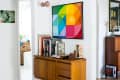 Mid-century modern console with books and decor, under a colorful geometric artwork, in a bright hallway.