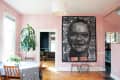 Dining room with pink walls, large portrait tapestry, round table, wooden chairs, and potted plants.