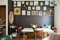 Dining area with a white table, wooden chairs, and a gallery wall of framed art and photos on a dark accent wall.