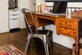 Home office with wooden desk, metal chair, laptop, desk lamp, and large dog portrait on the wall.