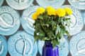 Blue vases with yellow flowers on wooden table, caviar-themed wallpaper in background.