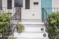 Front porch with turquoise door, house number 4023, black shutters, potted plants on steps, and iron railings.