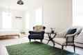 Bright bedroom with a navy armchair, white armchair, round table, and green rug.