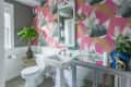 Bathroom with vibrant pink and gray leaf-patterned wallpaper, white sink, toilet, and a potted plant on a wicker stand.