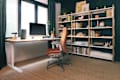 Modern home office with a wooden desk, ergonomic chair, computer, and a bookshelf filled with books and decor.