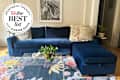 Navy blue velvet Sloan chaise sleeper storage sectional sofa with plush cushions, a glass coffee table, and a colorful floral rug. A zebra print hangs on the wall.