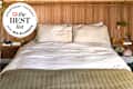Cozy bed with white and green bedding, wooden headboard, and bedside shelf with books and plants.