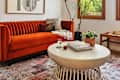 Living room featuring an orange velvet sofa, round coffee table, books, a glass of water, and potted plants.