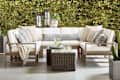 Outdoor seating area featuring a sectional sofa with cream cushions, decorative pillows, and a glass-top coffee table.