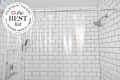 White tile and black grout shower with clear curtain liner. Seal in upper left corner reads "Apartment Therapy The Best List: 2023 Shower Curtain Liners"