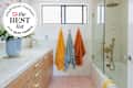 Bright bathroom featuring a light wood vanity, colorful towels hanging, and a glass shower with gold fixtures. Seal in upper left: "Apartment Therapy The Best List Bath Towels 2026"